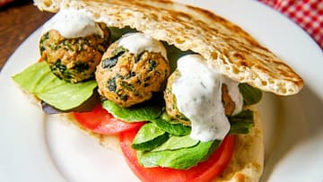 spinach turkey meatballs served in a sandwich with tomato, some greens, and alfredo sauce