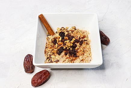 Oatmeal served in a white bowl, and topped with raisins and nuts