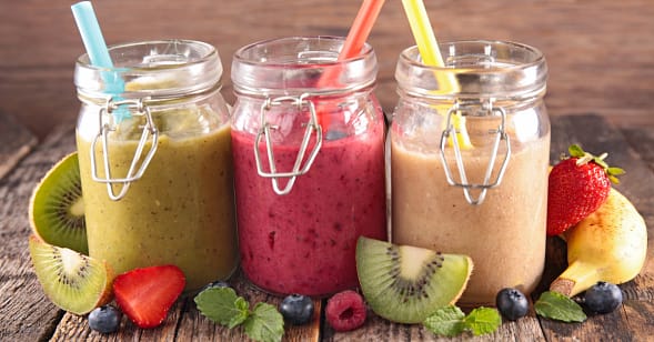 Three jars full of colorful smoothies with strawesand with fruits on the side