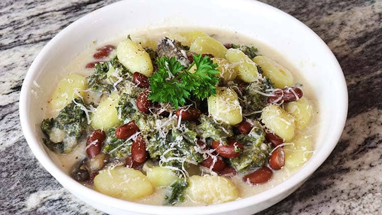 kale gnocci served in a white bowl and topped with some parsley and shredded cheese
