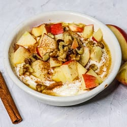 apple cinnamon yogurt served in a white bowl, topped with apples and nuts