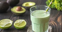 Glass full of green smoothie, avocado and limes on the side