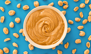 Peanut butter in a white bowl and some peanuts around