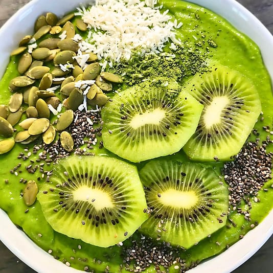 Green matcha smoothie bowl with kiwi, coconut, pumpkin seeds, and chia