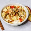 apple cinnamon yogurt served in a white bowl, topped with apples and nuts