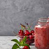 red smoothie served in a jar with a straw, and some cherries in the bowl on the side