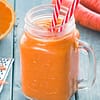 Orange smoothie served in a jar with two straws, and some carrots and oranges on the side