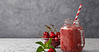 red smoothie served in a jar with a straw, and some cherries in the bowl on the side