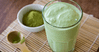 πράσινο smoothie σερβιρισμένο σε ποτήρι και μικρό μπολ γεμάτο σκόνη matcha στο πλάι