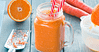 Orange smoothie served in a jar with two straws, and some carrots and oranges on the side