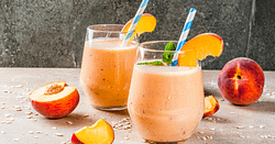 Two glasses full of orange smoothie, garnished with a straw and slice of a peach