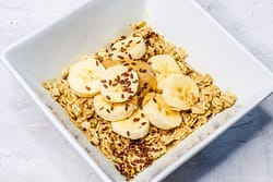 Oatmeal served in a white bowl, and topped with banana slices and peanut butter
