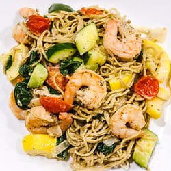 edamame linguins mixed with shrimps, zucchini, and tomatoes, served on a white plate