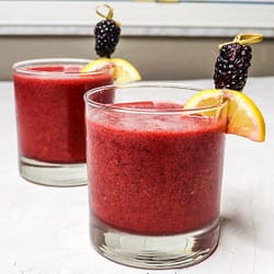 frozen blackberry lemonade served in two glasses, garnished with a piece of lemon, and one blackberry