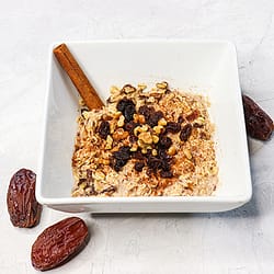 Oatmeal served in a white bowl, and topped with raisins and nuts