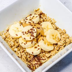 Oatmeal served in a white bowl, and topped with banana slices and peanut butter