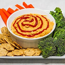 Mango Sriracha Hummus served in a white bowl with some carrots, broccoli and creckers on the side