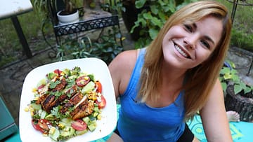 Caitlin smiles and holds white plate with grilled chicken and lot of vegetables