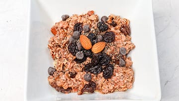 oatmeal served in a white bowl topped with chocolate chips, dried cherries, and almonds