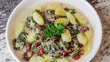 Kale gnocchi served in white bowl and topped with parsley leaves and shredded cheese