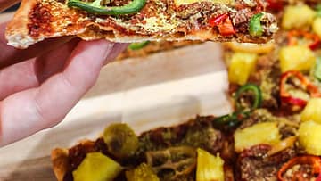 A hand holding a Pineapple Pepper Plant-based Pizza slice