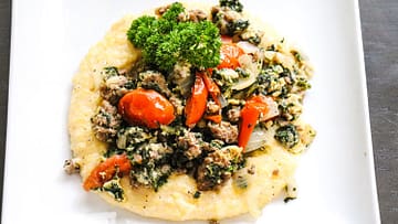 The white plate with creamy grits served with some greens and tomatoes on the top,