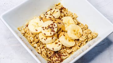 Oatmeal served in a white bowl, and topped with banana slices and peanut butter