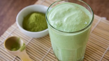 green smoothie served in a glass and small bowl full of matcha powder on the side
