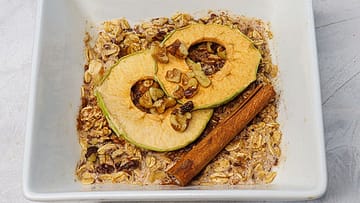 Oatmeal served in a white bowl topped with cinnamon stick and dried apple rings