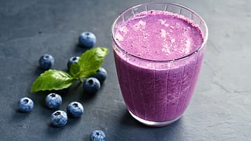 purple smoothie served in a glass and some blueberries on the side