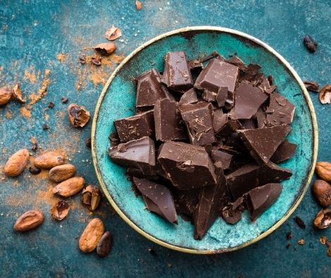 crushed dark chocolate served in a blue plate with some cocoa beans