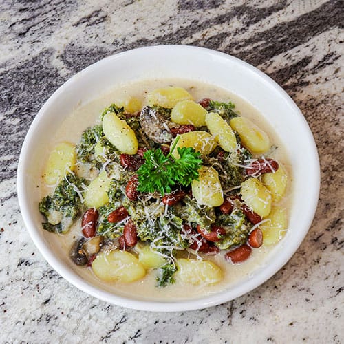 Kale gnocchi served in white bowl and topped with parsley leaves and shredded cheese