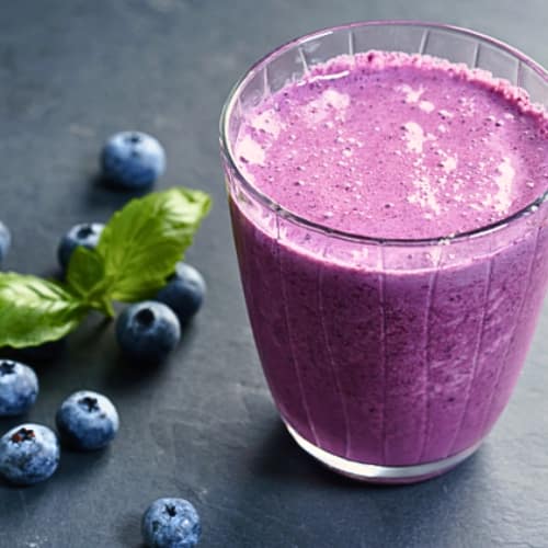 purple smoothie served in a glass and some blueberries on the side