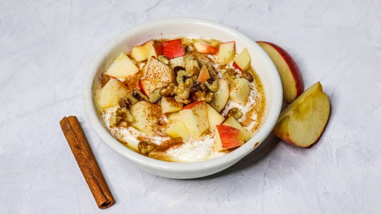 apple cinnamon yogurt served in a white bowl, topped with apples and nuts