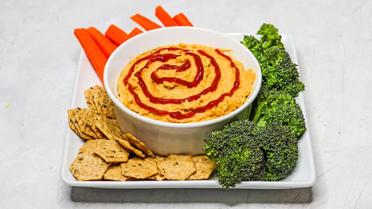 Mango Sriracha Hummus served in a white bowl with some carrots, broccoli and creckers on the side