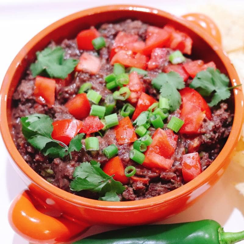 jalapeno black bean served with some onions and tomatoes on the top in a nice ceramic bowl