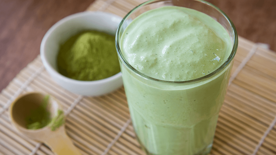green smoothie served in a glass and small bowl full of matcha powder on the side