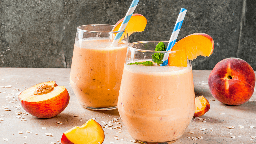 Two glasses full of orange smoothie, garnished with a straw and slice of a peach