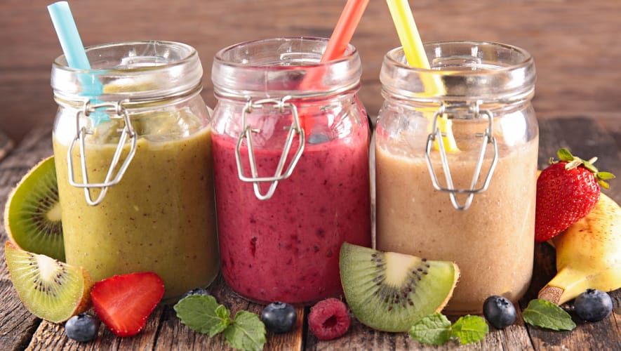 Three jars full of colorful smoothies with strawesand with fruits on the side